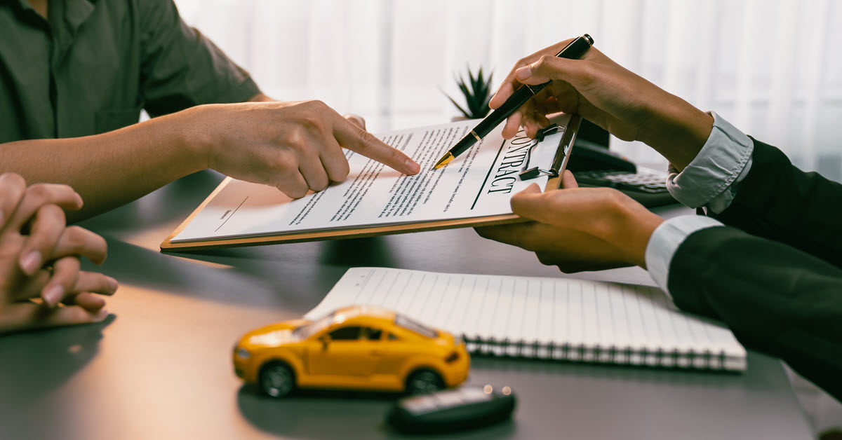 The hands of a loan officer holds an auto loan contract while a member points to a paragraph of it